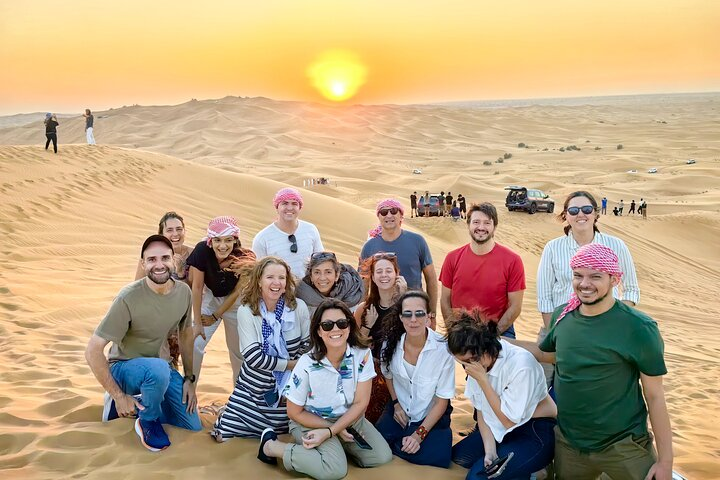 Experience the Arabian Desert with a group of adventurers surrounded by stunning sand dunes and a breathtaking sunset perfect for creating unforgettable memories.